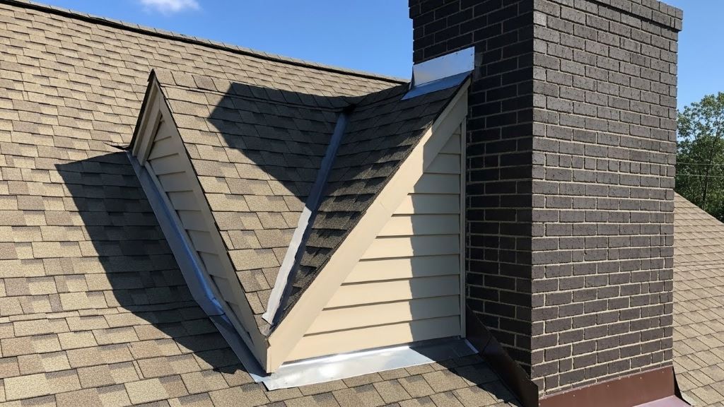 Triangular chimney cricket installed behind brick chimney on asphalt shingle roof diverting water